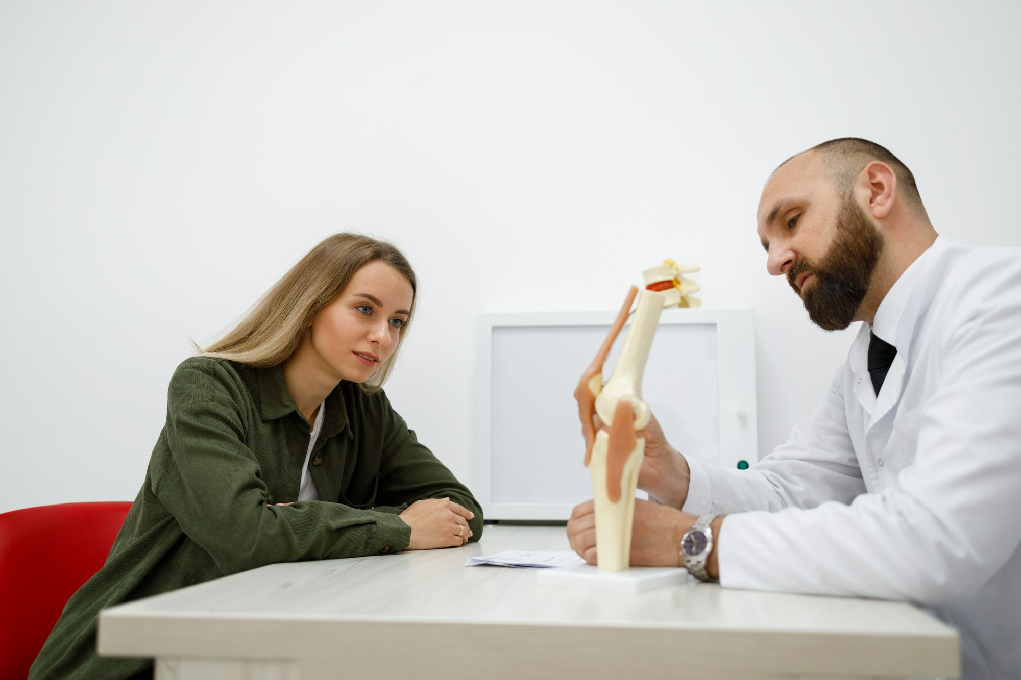 Male doctor showing knee joint model to woman patient and explains the cause of his pain